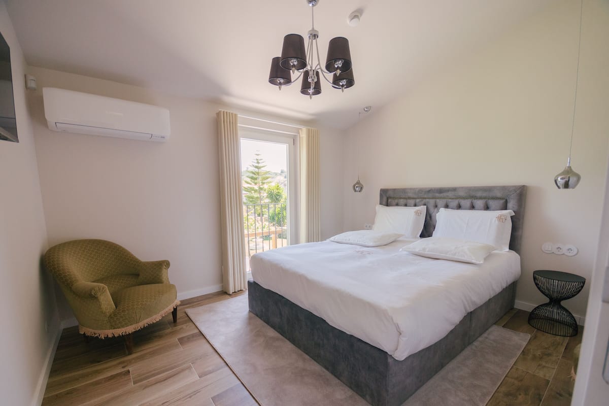 A bedroom with a large bed, a chair, a window, and an air conditioning unit.