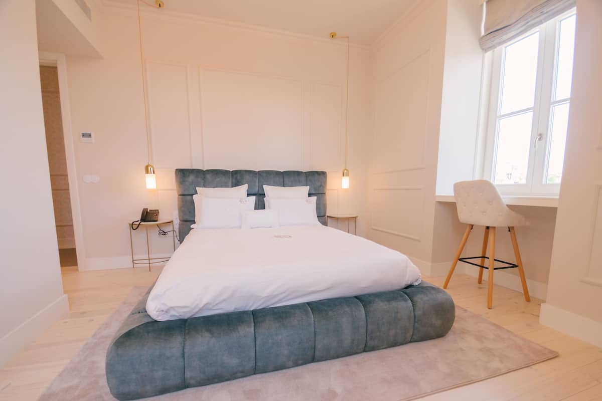 A modern bedroom with a large bed, bedside lamps, a desk, and a window.