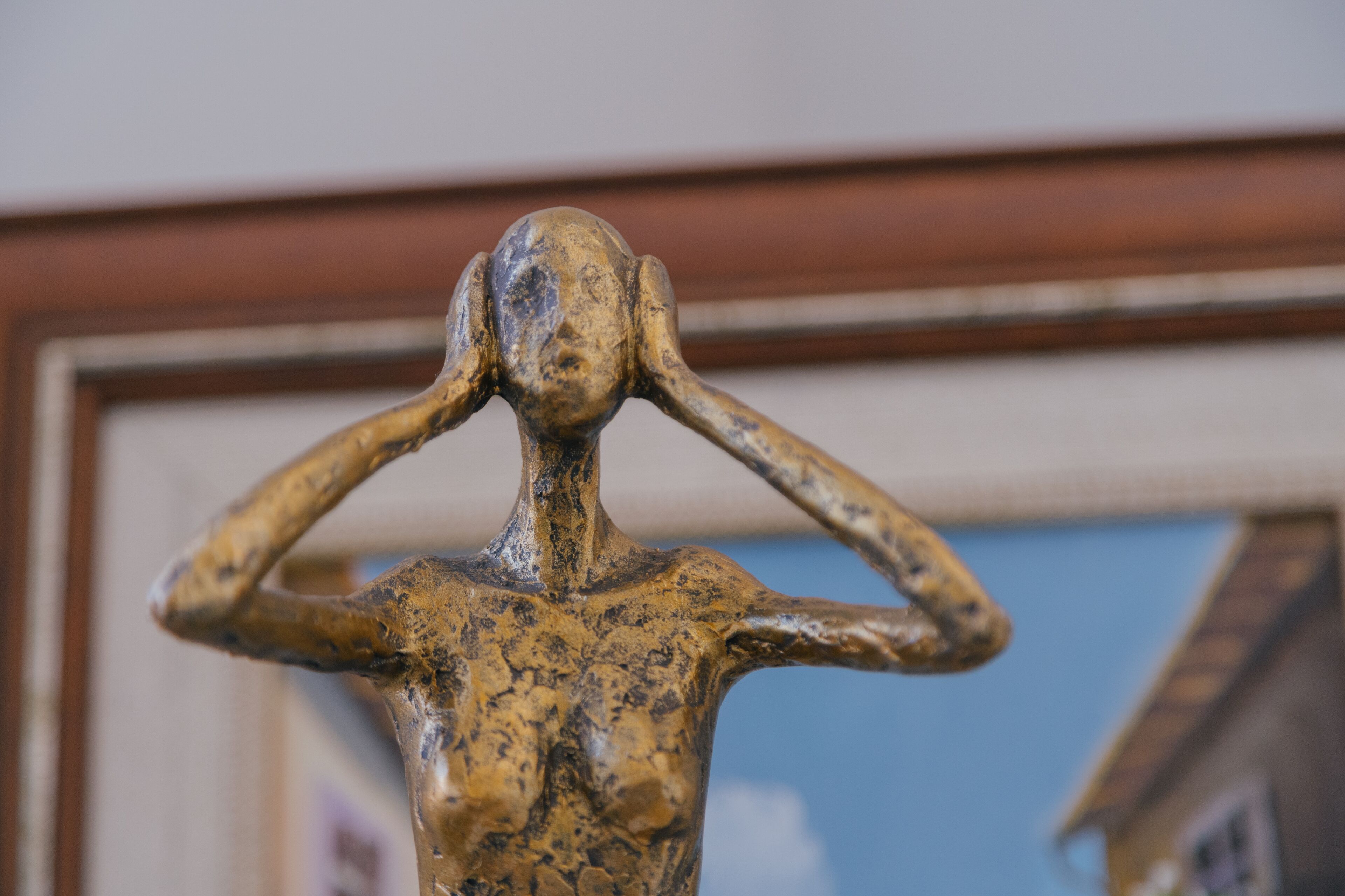 Eine Statue mit einer menschlichen Figur, wobei die Hände das Gesicht verbergen, und verschwommener Hintergrund.