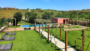 Un espace piscine agrémenté d’une pergola, de chaises longues et d’un bâtiment rouge, le tout situé dans un cadre de vignoble.