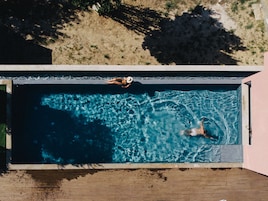 Vista aérea de una piscina rectangular con agua azul cristalina, rodeada por una terraza de madera y una zona verde.