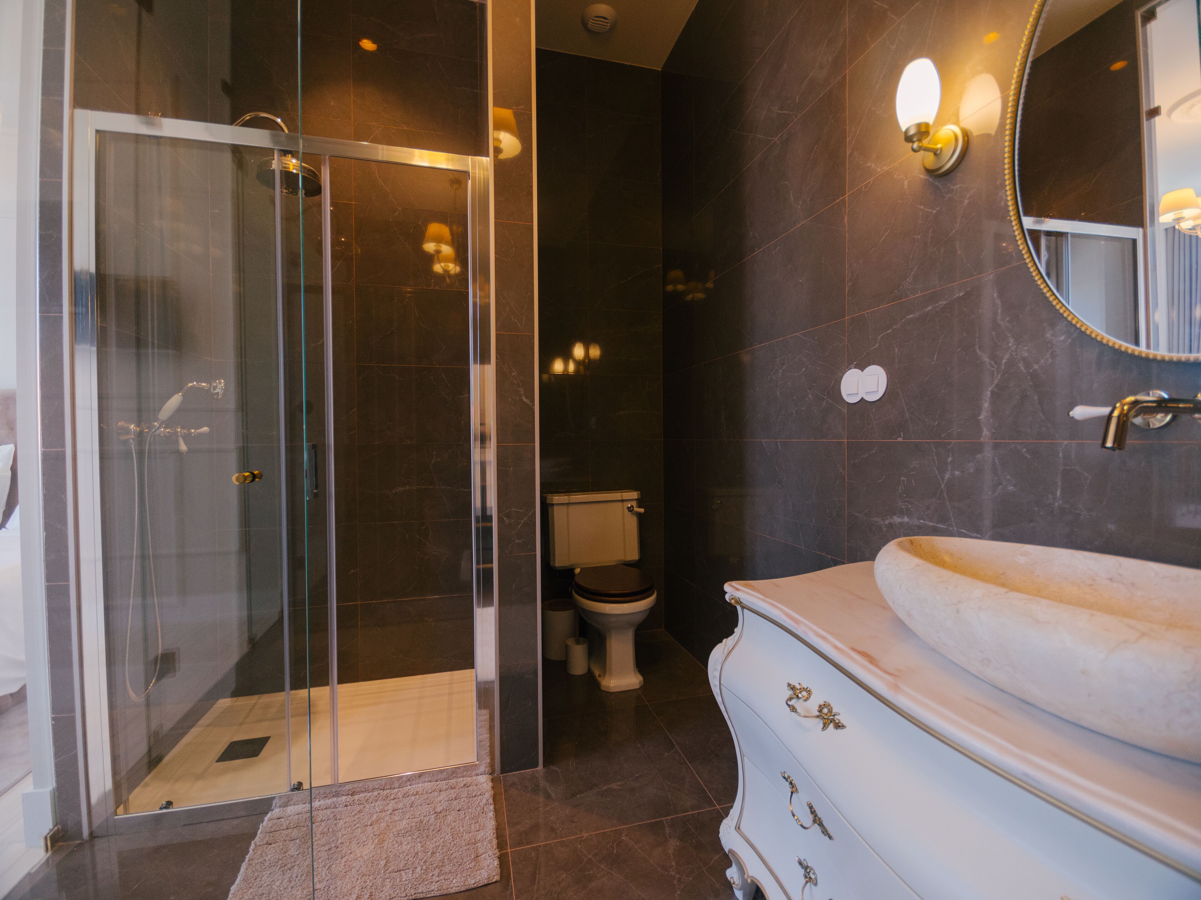 Une salle de bain moderne avec une douche à parois de verre, un meuble-lavabo blanc doté de poignées dorées et un mur recouvert de marbre foncé.