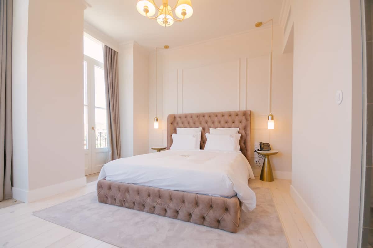 A spacious bedroom with a large bed, a chandelier, and a bedside table with a phone.