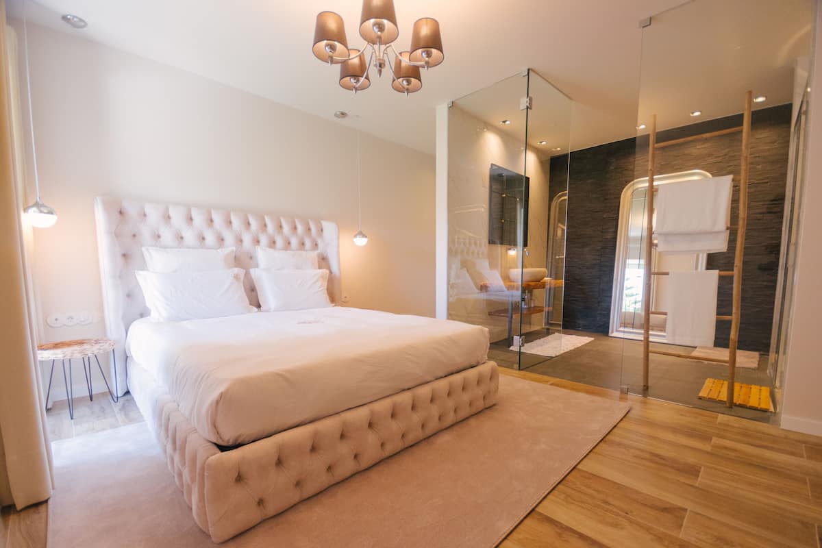 A modern bedroom with a large bed, a glass shower enclosure, and a wooden floor.