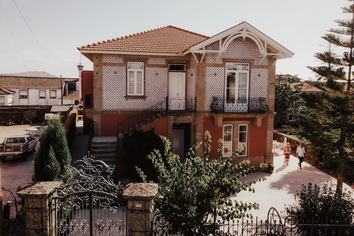 A two-story house with a tiled roof, a balcony, and a garden area.