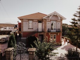 A two-story house with a tiled roof, a balcony, and a garden area.