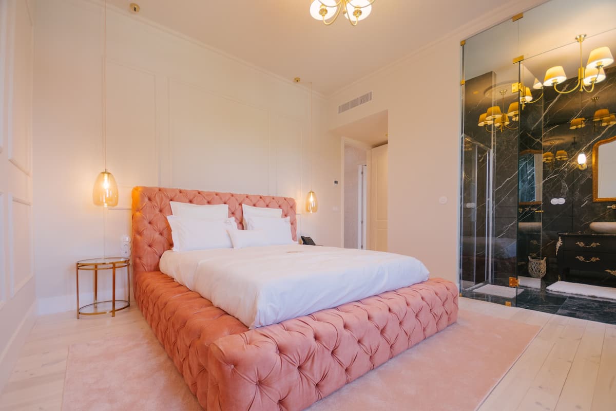 A bedroom with a large bed, a glass shower enclosure, and a marble-tiled bathroom.