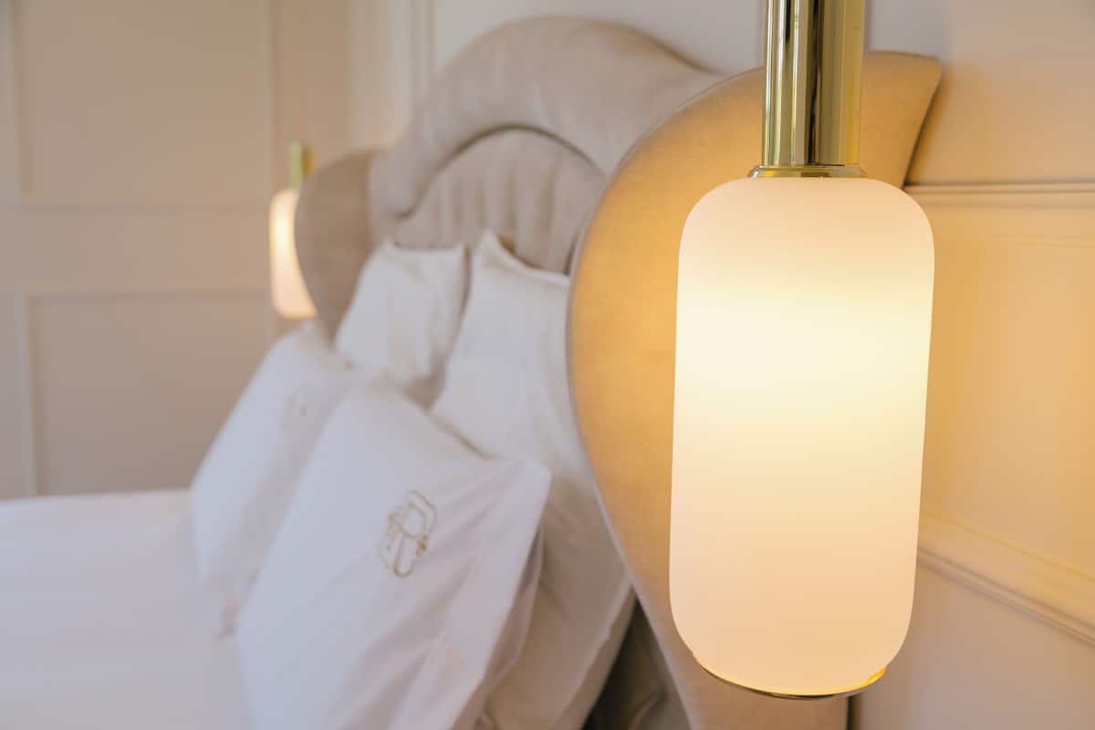 A bed with white linens and a headboard with a light fixture.