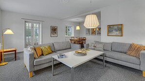 A modern living room with a grey sofa, a white coffee table, and a dining area with a wooden table and chairs. - 6 bedroom gorgeous home in Kværndrup (Kværndrup)