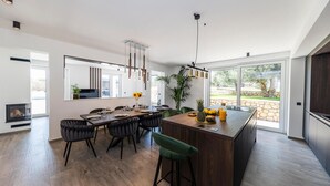 Une cuisine moderne dotée d'un îlot central, d'un coin repas avec des chaises et de grandes fenêtres offrant une vue sur l'extérieur.