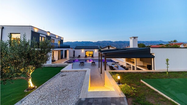 Une maison moderne dotée d’une piscine, d’un espace salon extérieur et offrant une vue sur les montagnes.
