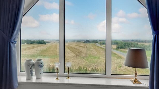 A room with a large window offering a view of a rural landscape, a vase, and two candle holders on the windowsill. - Gorgeous home in Lemvig with WiFi (Lemvig)