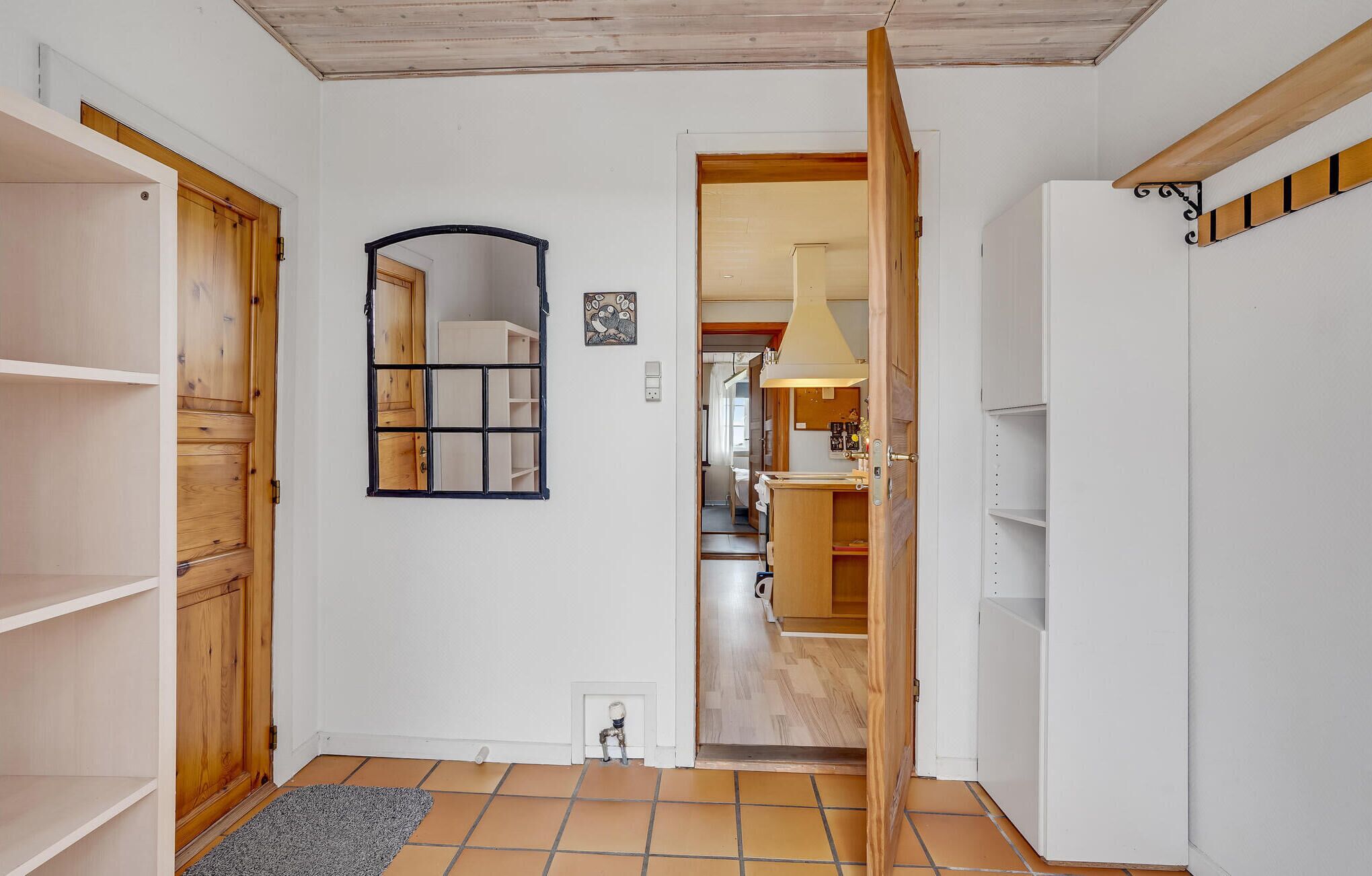 A hallway with wooden doors, a tiled floor, and a mirror on the wall.