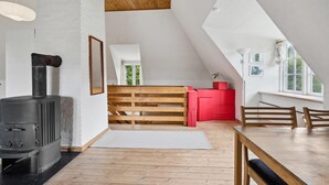Una habitación de buhardilla acogedora con estufa de leña, un banco de madera, una mesa de comedor y un armario rojo.