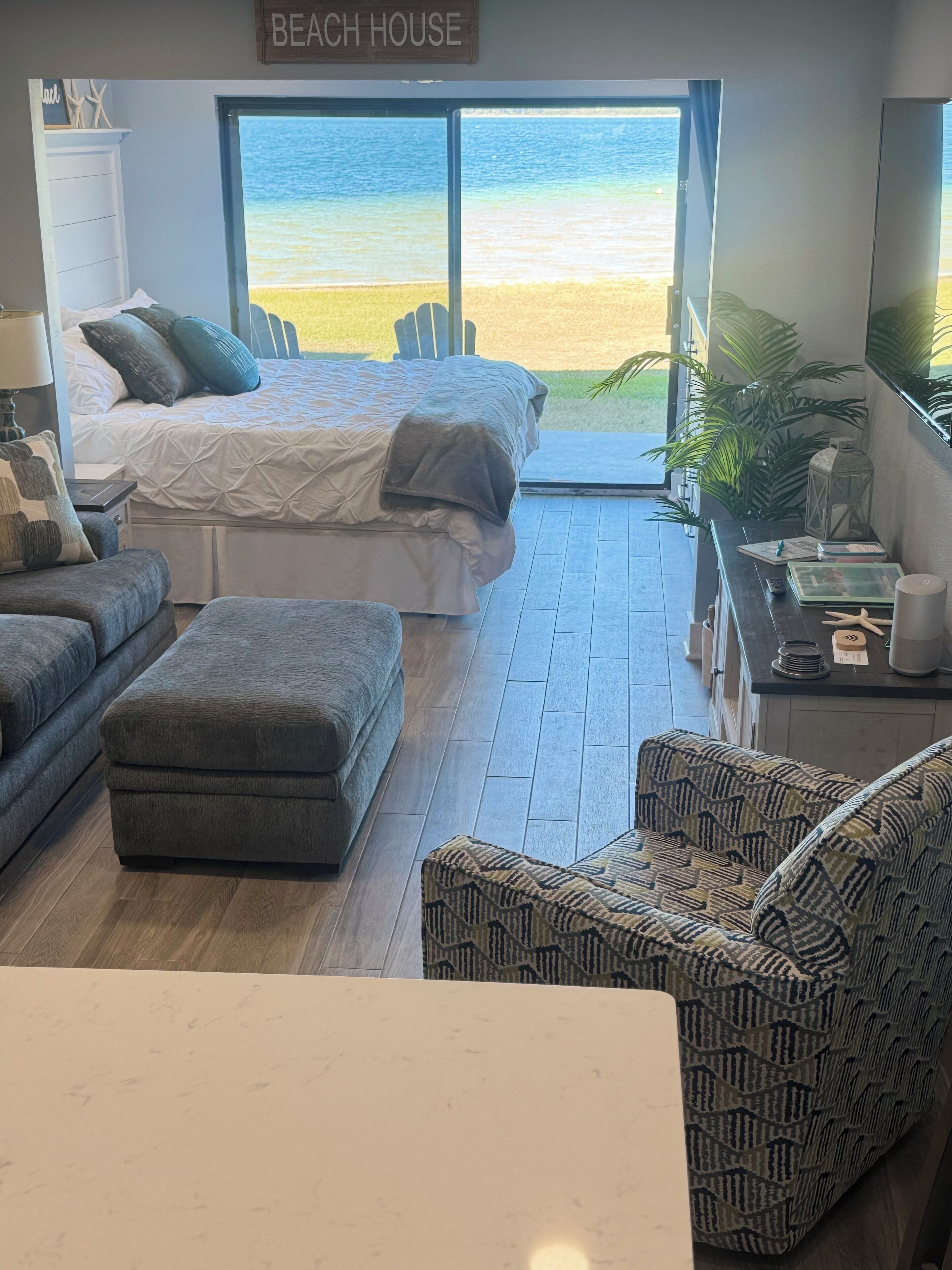 A beach-themed room with a bed, a sofa, an ottoman, and a view of the beach.
