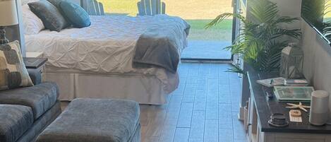 A beach-themed room with a bed, a sofa, an ottoman, and a view of the beach.