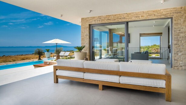 A modern outdoor living area with a wooden bench, a pool, and a view of the sea.