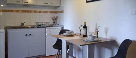 Una cocina compacta con armarios blancos, salpicadero de azulejos y un comedor con mesa dispuesta para dos.