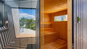 Una sauna con paredes de madera y una ventana, suelo de hormigón y vistas a un jardín y una casa.