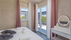 Un dormitorio con una cama, una mesita de noche con espejo y vistas al exterior a través de un ventanal corredero.
