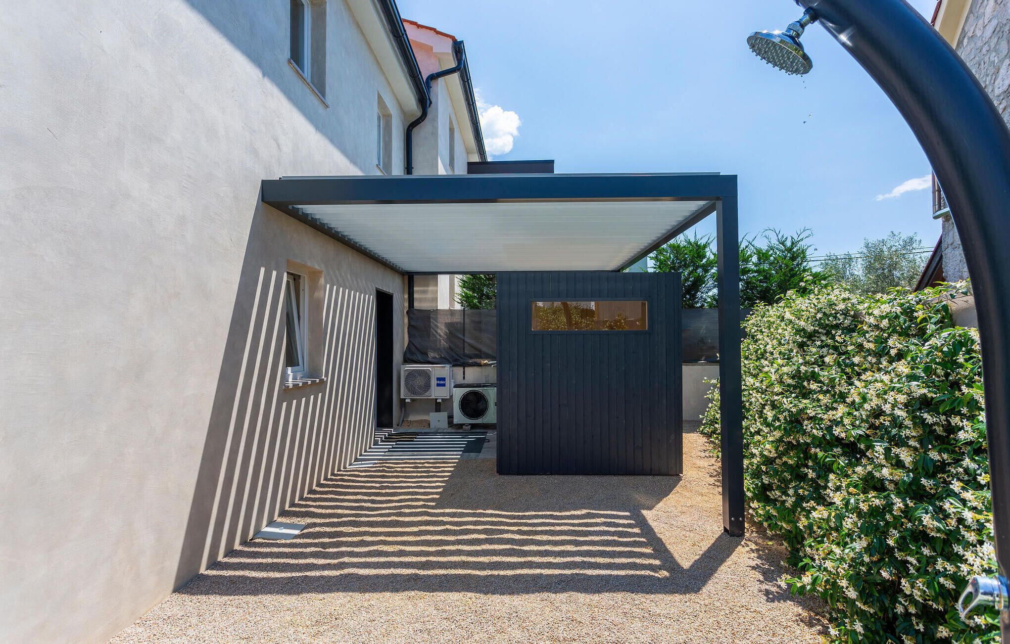 Een modern buitengebied met een overdekte doorgang, een klein afgesloten gedeelte met een deur en een airconditioner.