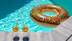 Una piscina con un flotador con forma de dona y dos vasos de jugo de naranja.