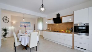 Une cuisine moderne avec des meubles blancs, un four encastré et un coin repas avec une table dressée pour deux personnes.
