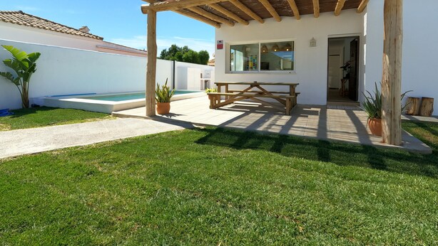 A covered patio with a wooden table and chairs, a small pool, and a white building with a window. - Villa Muscari Nature 200 meters from the beach 10 pax (Los Caños de Meca)
