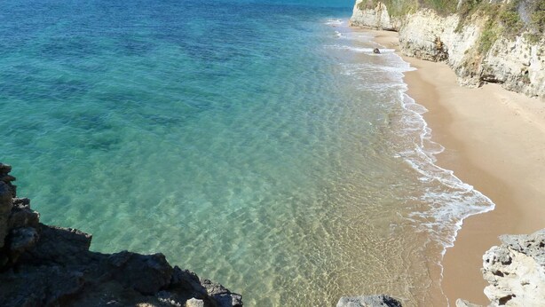 A coastal beach with clear waters, a sandy shore, and rocky cliffs.