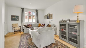 A living room with a sofa, armchairs, a coffee table, a patterned rug, a bookshelf, and a window with curtains. - 3 bedroom nice home in Kværndrup (Kværndrup)