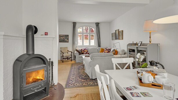 A cozy living room with a fireplace, a dining area with a table set for two, and a comfortable seating area with a sofa and armchairs. - 3 bedroom nice home in Kværndrup (Kværndrup)