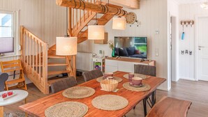 A wooden dining table with woven placemats, a wooden staircase, and a television in the background.