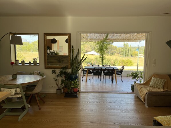 A cozy living room with a dining area, wooden flooring, and a large window offering a view of the outdoors.
