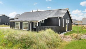 Une maison moderne à la façade noire, dotée d’un toit en pente, de grandes fenêtres et d’une cheminée bien visible.