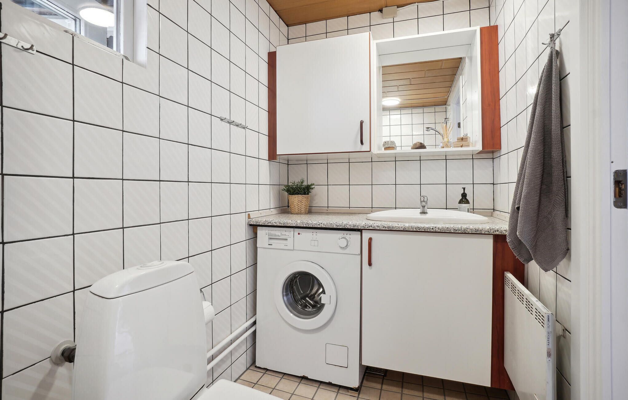 Una cocina compacta con azulejos blancos, lavadora, pileta y un ventanal pequeño.