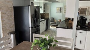 Une cuisine moderne avec un réfrigérateur noir, des armoires blanches et un coin repas comprenant une table et des chaises en bois.