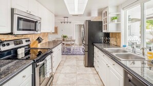 Une cuisine moderne avec des armoires blanches, un réfrigérateur en acier inoxydable, un four à micro-ondes et une cuisinière. On y trouve également un coin repas avec une table et des chaises, ainsi qu’une fenêtre qui laisse entrer la lumière naturelle.
