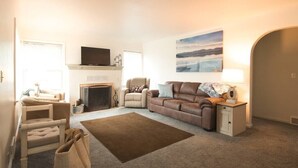Un salon avec une cheminée, un canapé en cuir marron, un fauteuil beige, un téléviseur et un tableau accroché au mur.