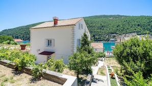 Un bâtiment blanc avec un toit recouvert de tuiles, un petit balcon et une vue sur une colline verdoyante.
