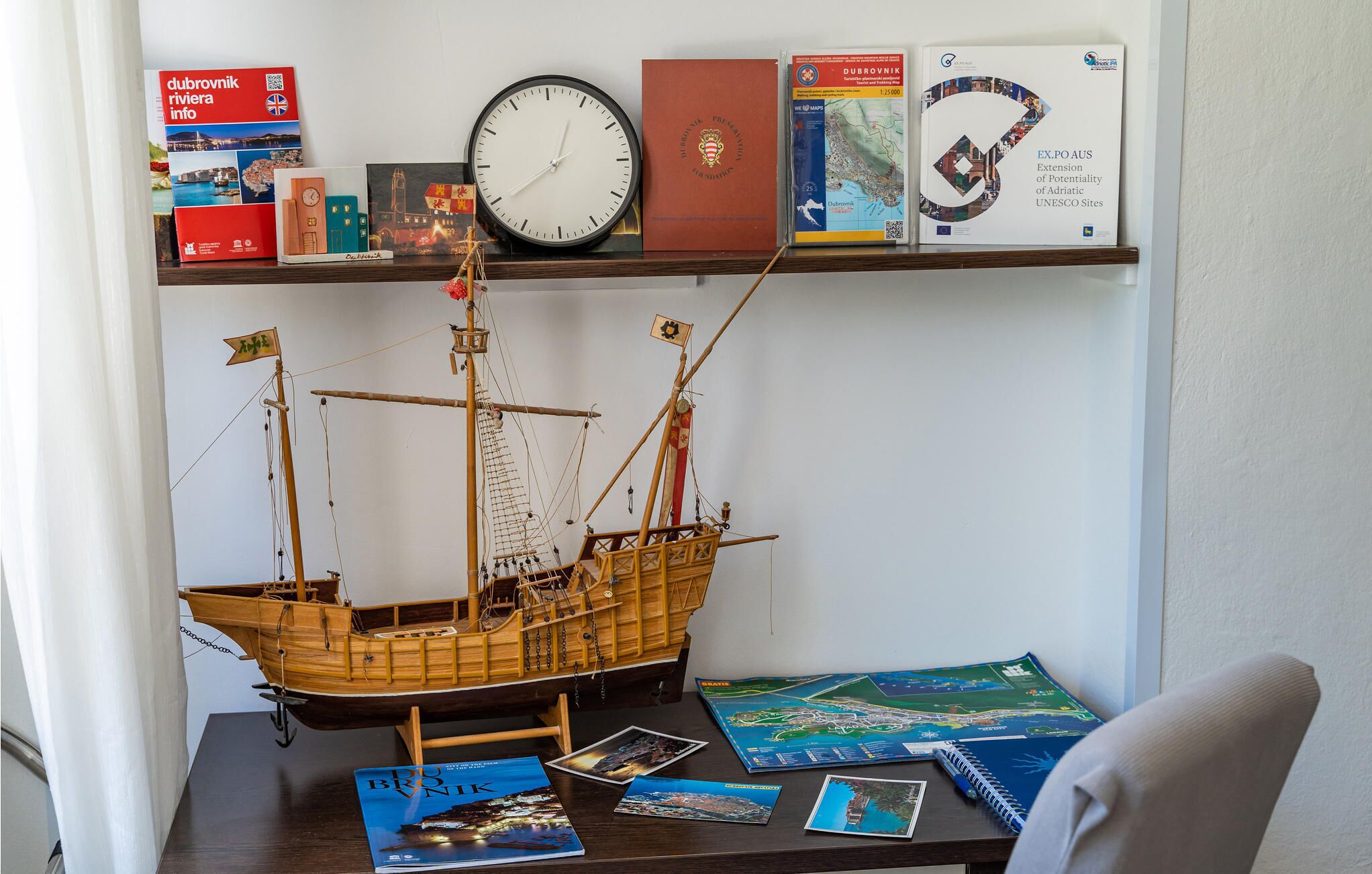 A desk with a model ship, books, a clock, and a map.