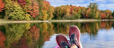 A view from a kayak on a calm lake with colorful autumn trees in the background.