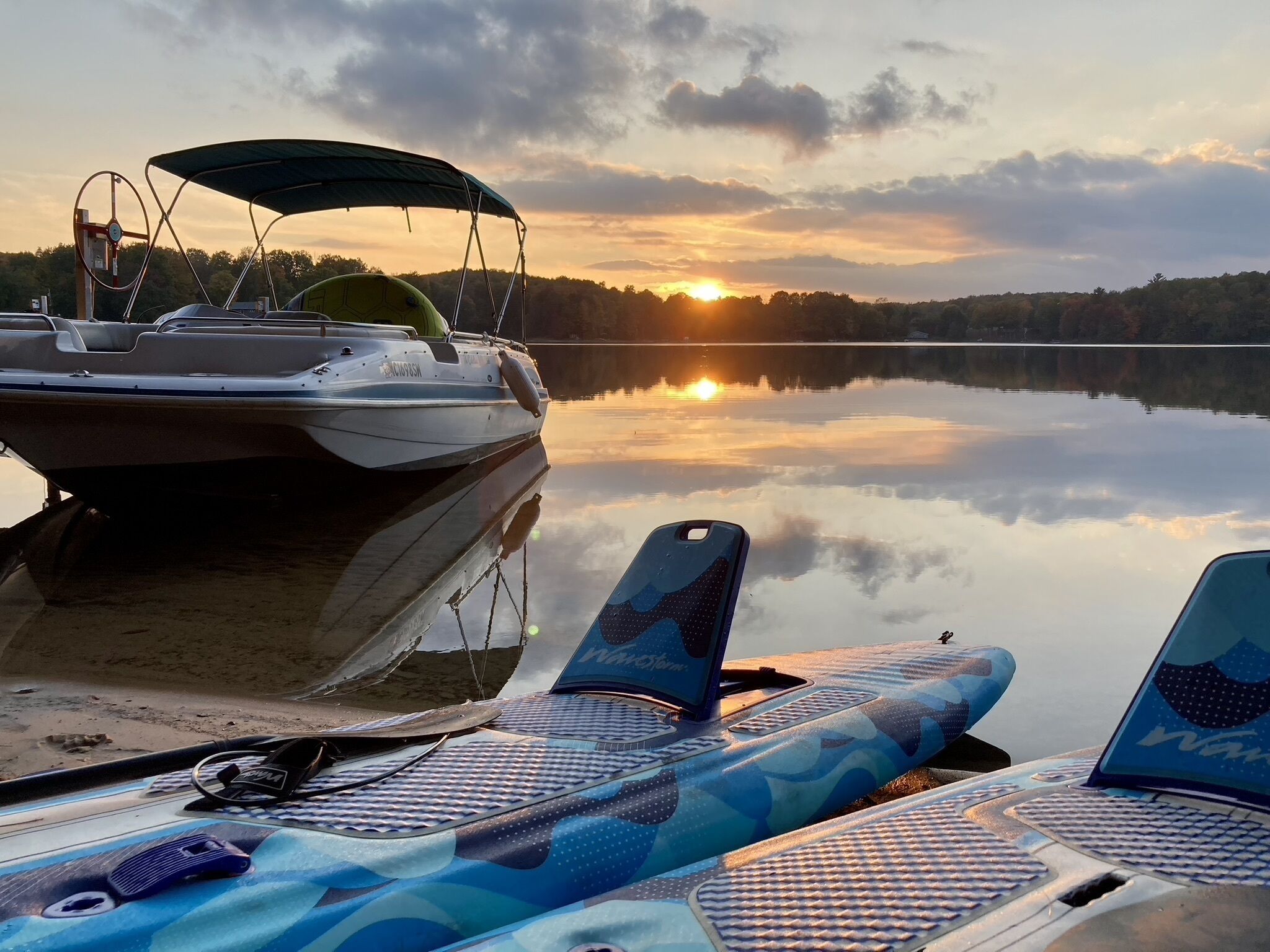 A boat docked at a calm lake with a sunset in the background.