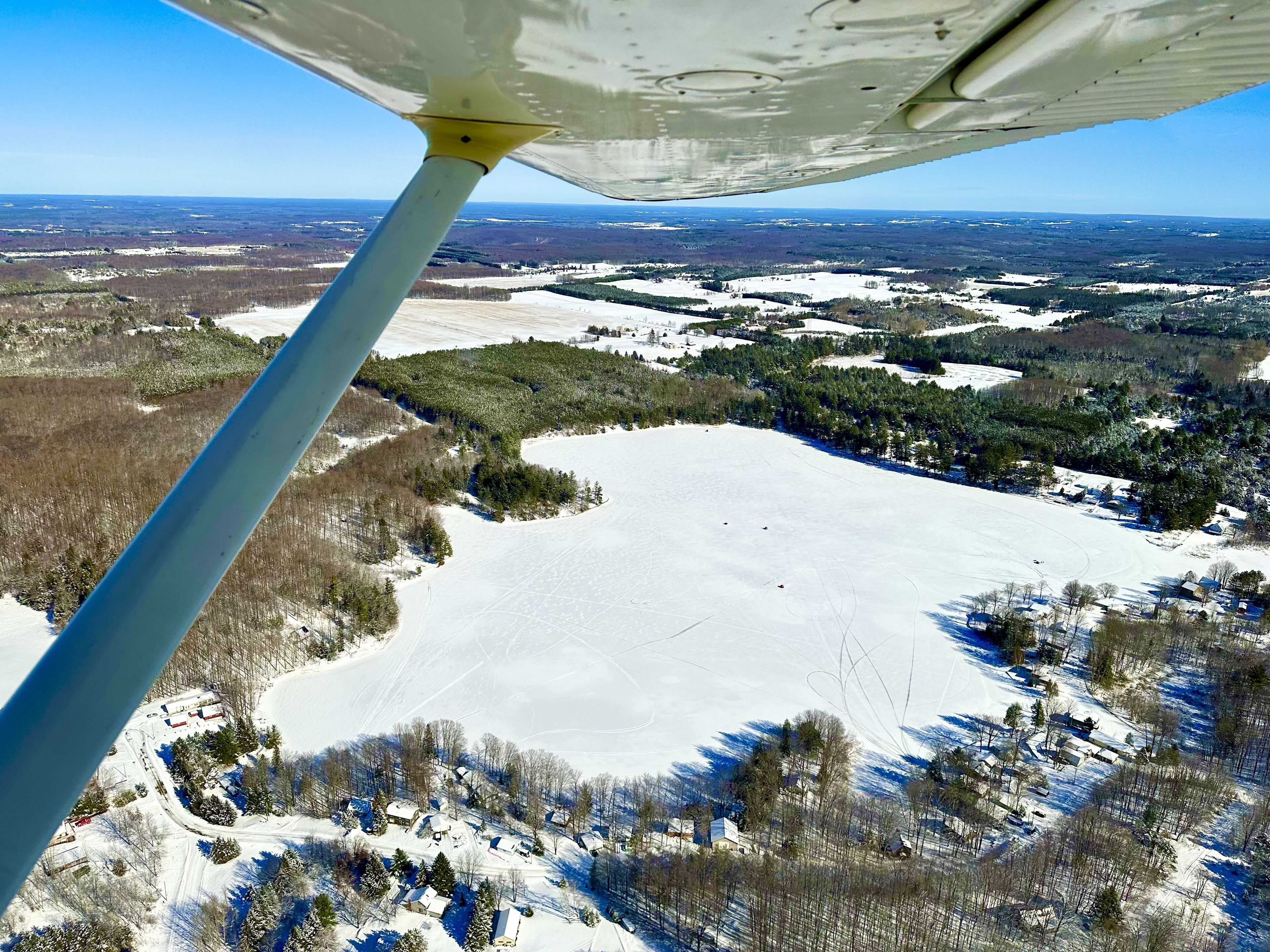 Een besneeuwd landschap met een groot open veld, verspreide bomen en enkele gebouwen.