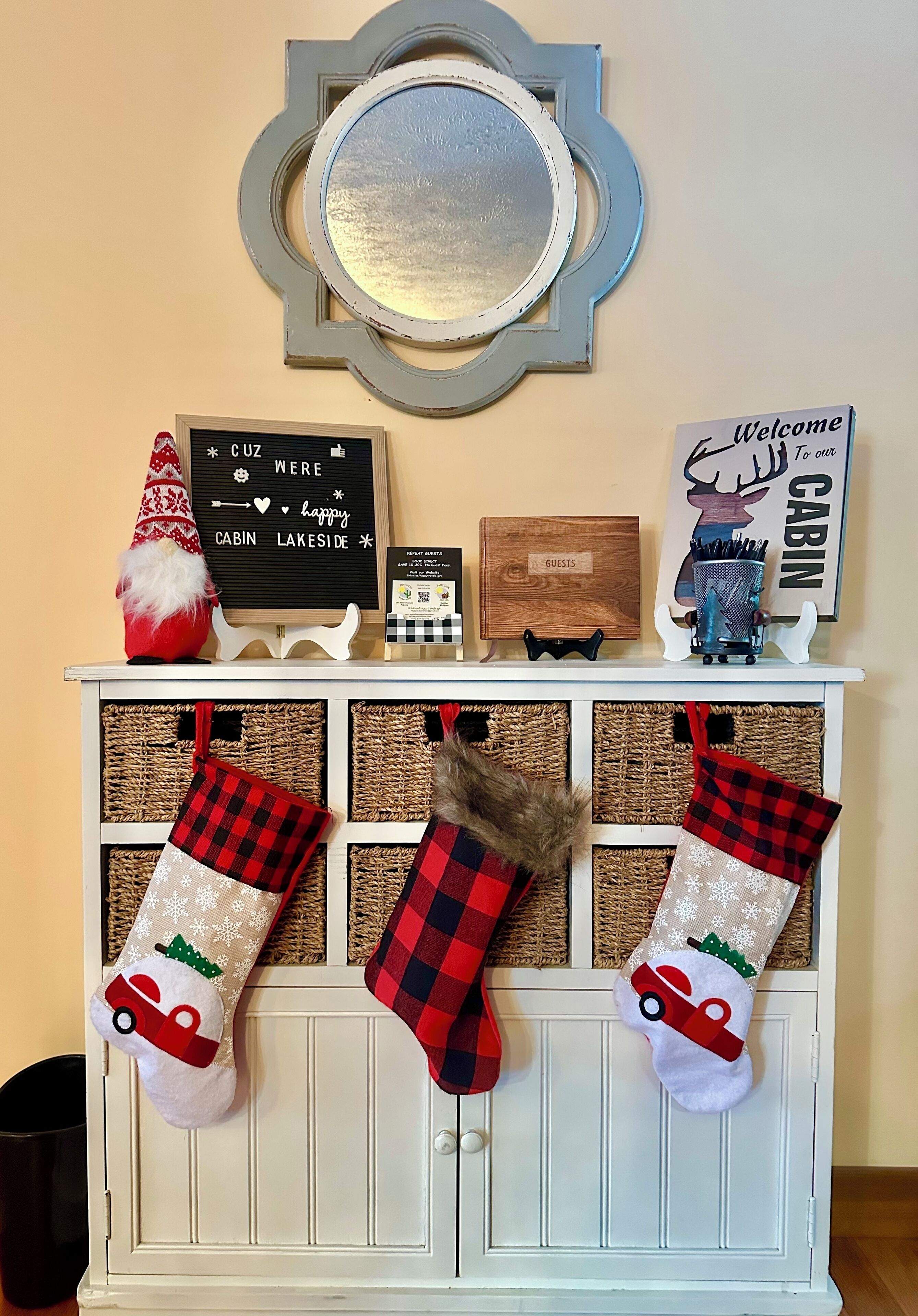 A cabin-themed display with a mirror, a welcome sign, a signboard, and two festive stockings.