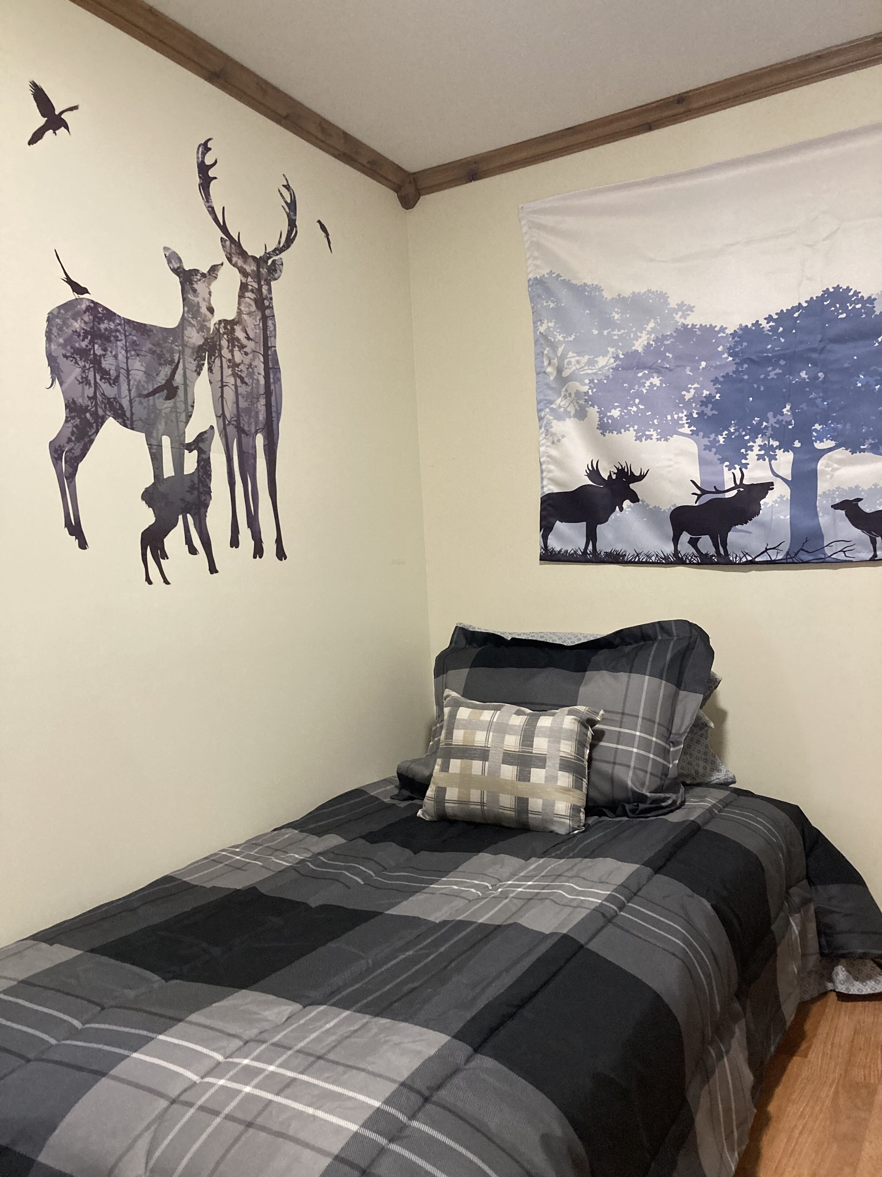 A bedroom with a bed, a wall mural of deer, and a window with a forest scene.