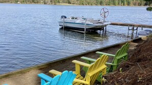 A lakeside dock with a rowboat and colorful Adirondack chairs. - Fall Splendor! Cozy Cabin, Lake Views & Campfires! (Cadillac)