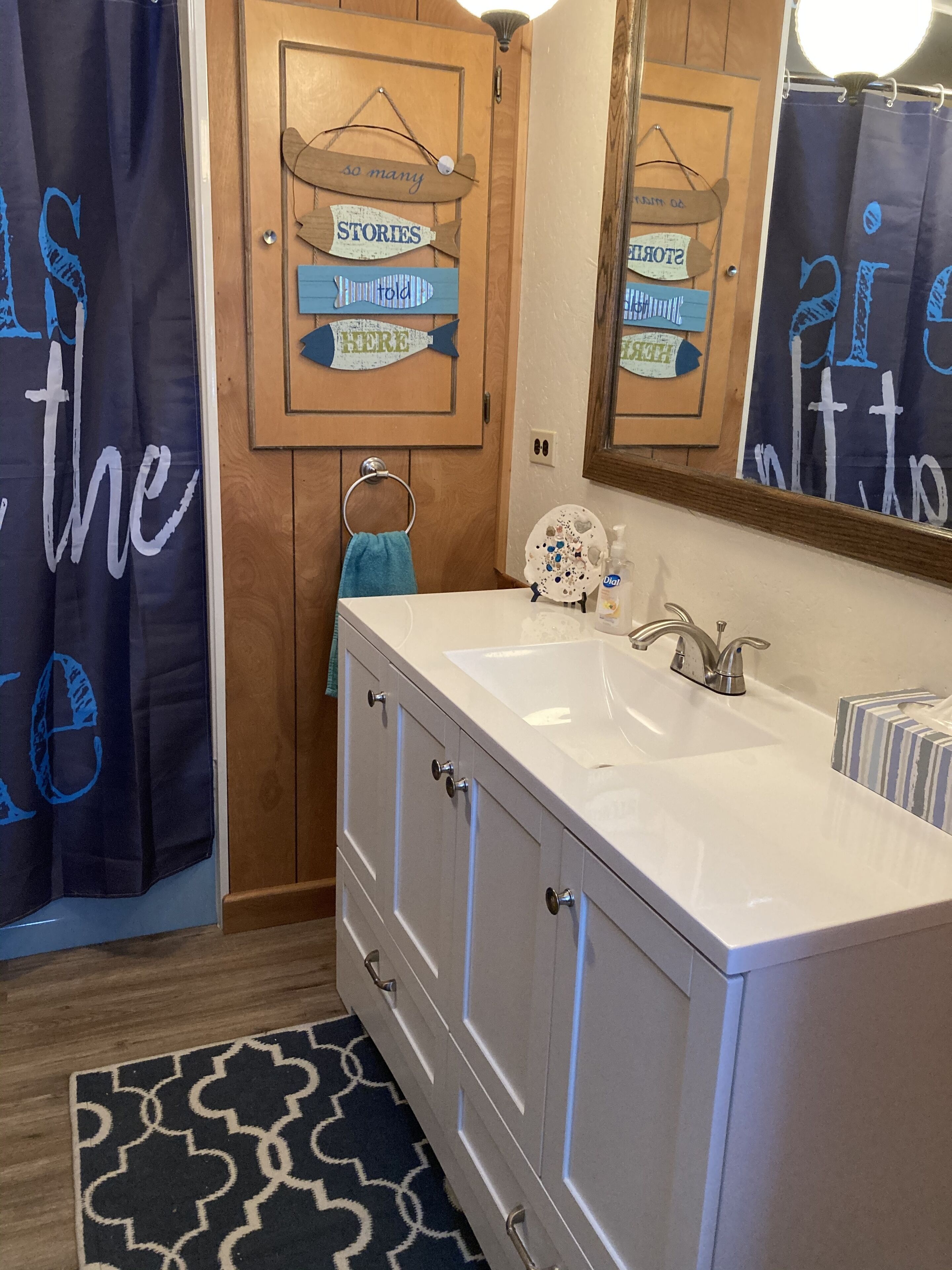 A bathroom with a white vanity, a mirror, and wooden doors. There are decorative signs on the doors and a blue shower curtain.