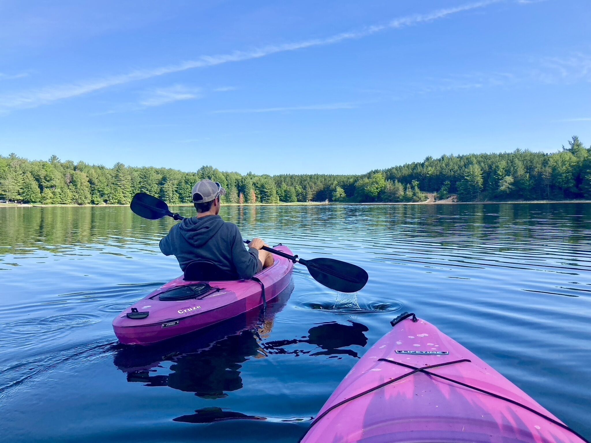A person kayaking on calm water with a forested shoreline in the background.