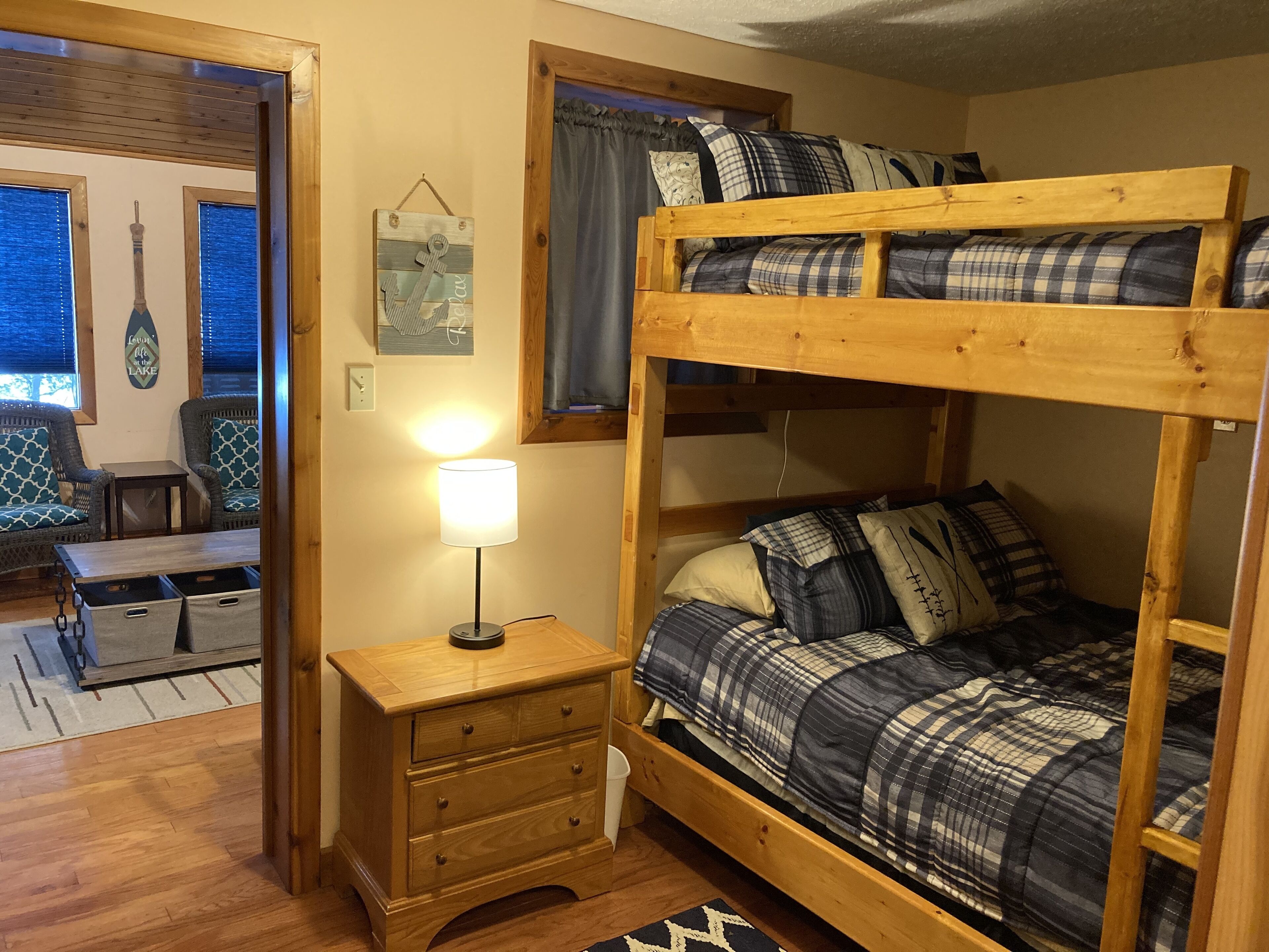 A bunk bed with plaid bedding, a bedside lamp, and a wooden nightstand with drawers.
