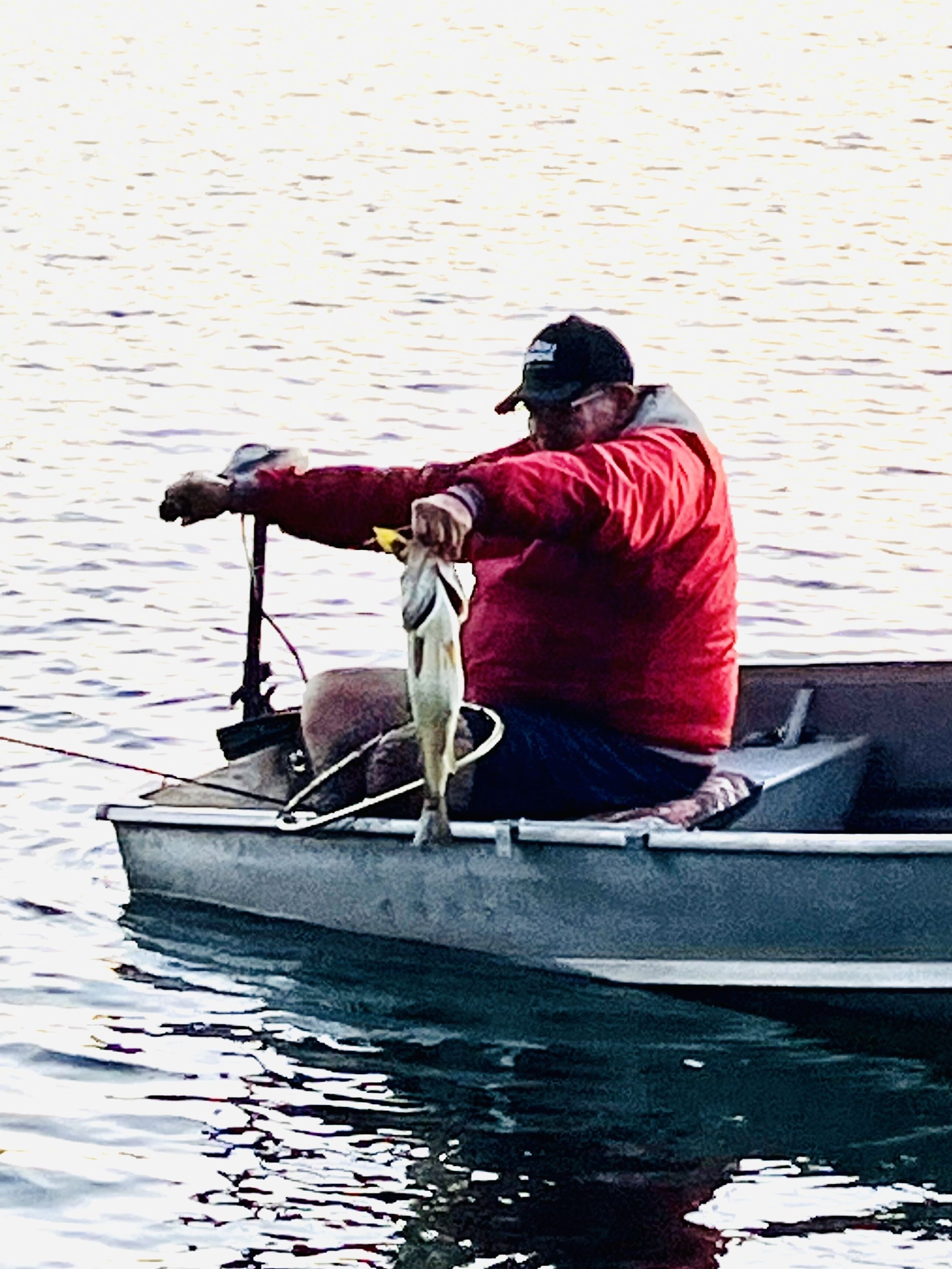 A man in a red jacket and cap fishing from a small boat.